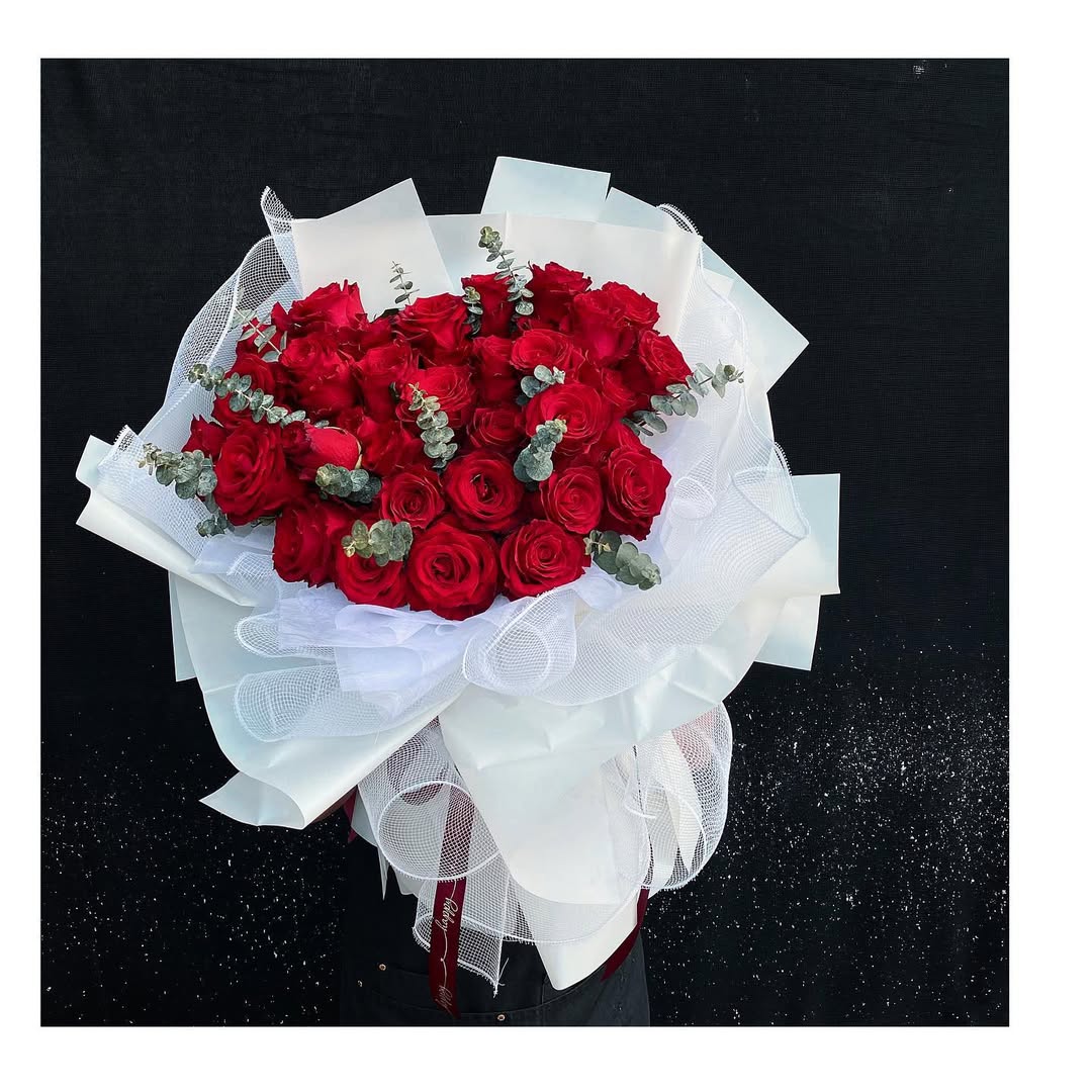 Velvety red roses with eucalyptus, beautifully gathered in layers of sheer white wrapping